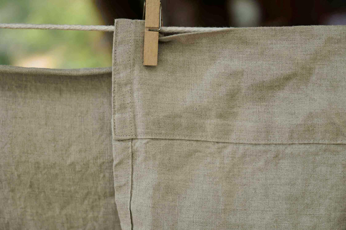 Natural linen fabric with subtle texture, hanging on a clothesline, ideal for apparel and home sewing projects.