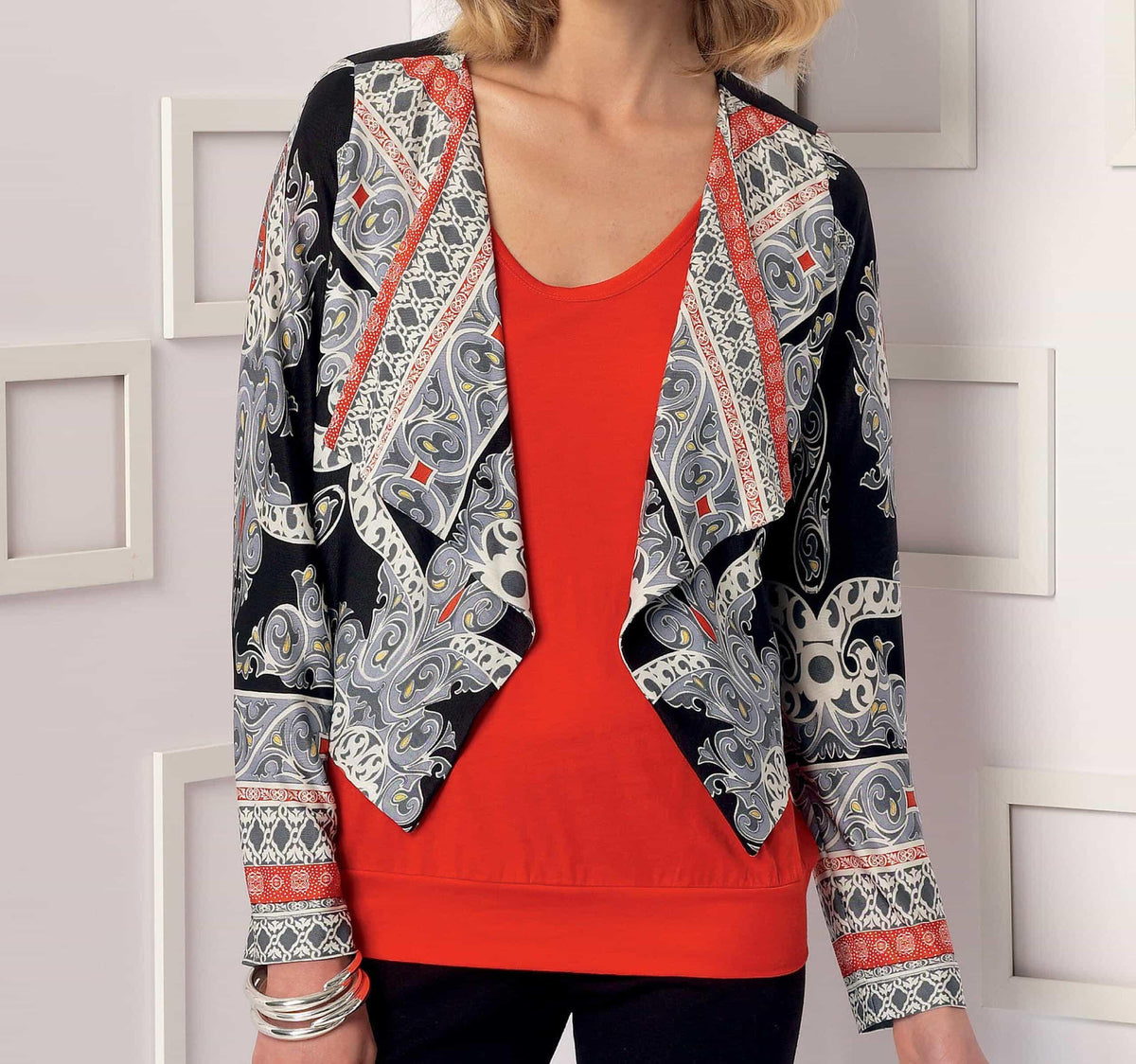 Woman wearing a stylish open-front cardigan with intricate paisley and geometric print in black, gray, white, and red, paired with a solid red top.