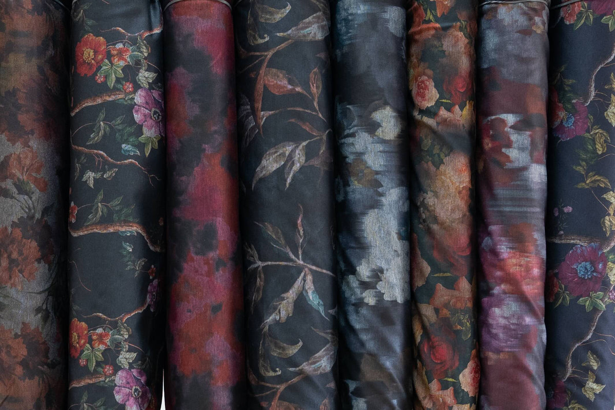 Rolls of dark floral and abstract printed fabric for apparel and quilting, featuring rich reds and botanical designs