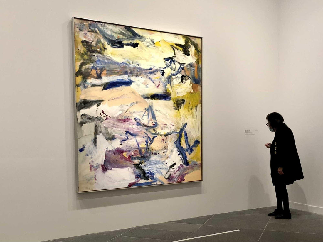 Woman viewing large abstract painting with bold brushstrokes in yellow, blue, and purple at art gallery