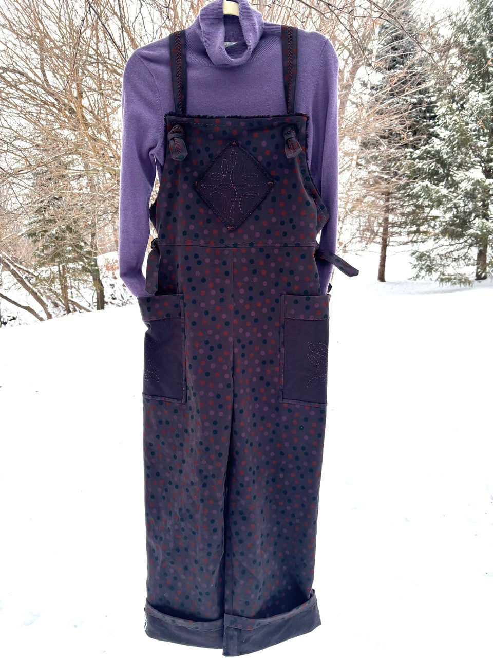 Purple polka dot overalls with embroidered patch, paired with turtleneck, displayed outdoors in snow