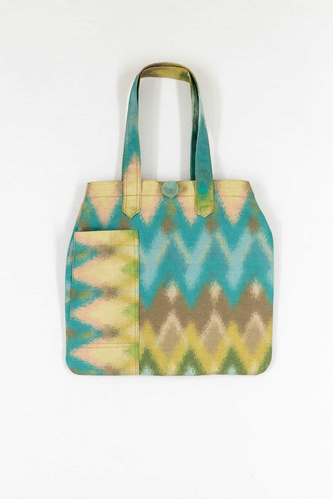 Handmade tote bag with colorful geometric ikat print, featuring front pocket and button closure, ideal for sewing projects.