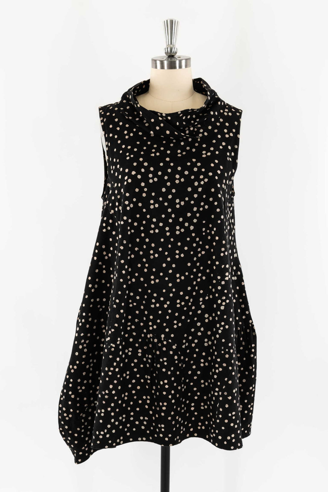 Black sleeveless dress with beige polka dots, cowl neck, and tiered hem on mannequin