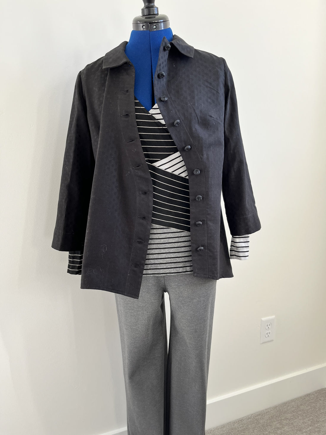 Dark gray button-up jacket over striped top and gray pants on mannequin, showcasing apparel fabric styling