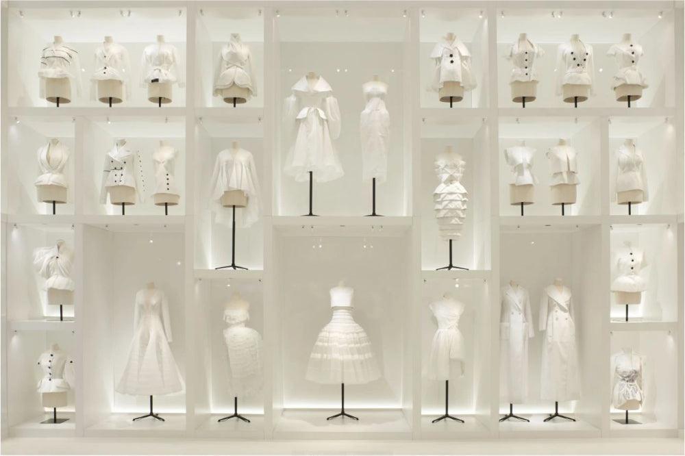 White designer garments displayed on mannequins in illuminated retail cubicles, showcasing fashion textiles and apparel sewing inspiration