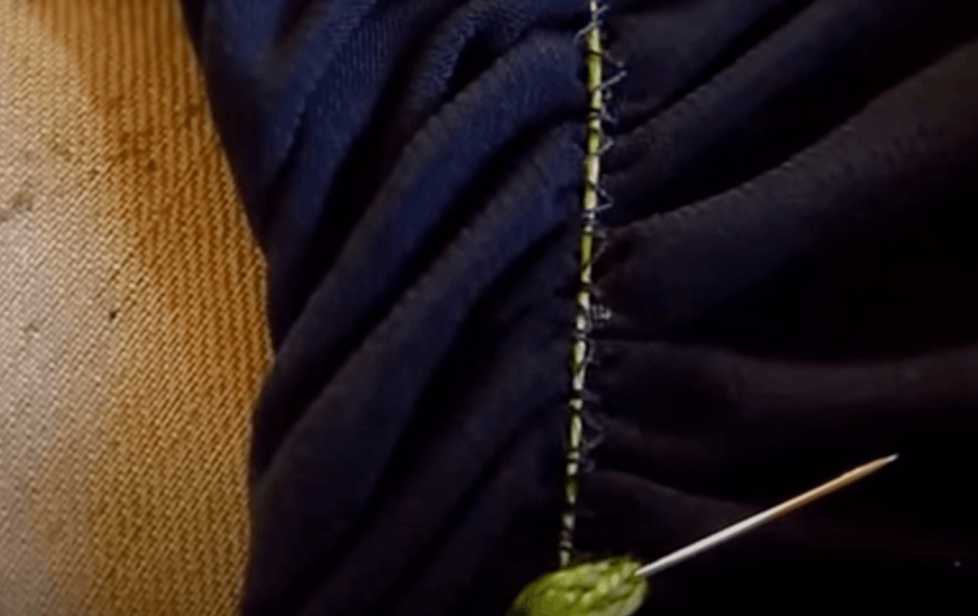 Close-up of dark blue fabric with green stitching and a pin, showcasing sewing detail for apparel or quilting projects.