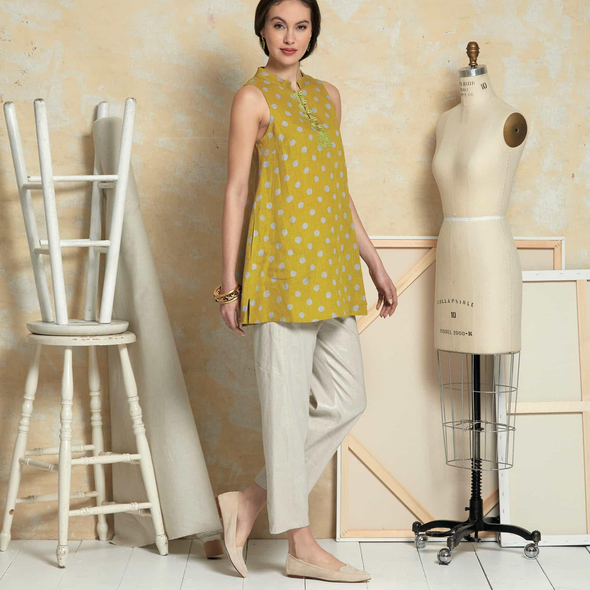 Woman in mustard yellow polka dot sleeveless top and linen pants, styled with mannequin and sewing studio decor
