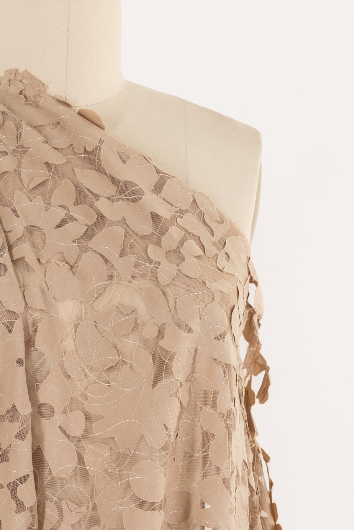 Beige floral lace fabric with leaf cutouts, ideal for apparel sewing and fashion projects
