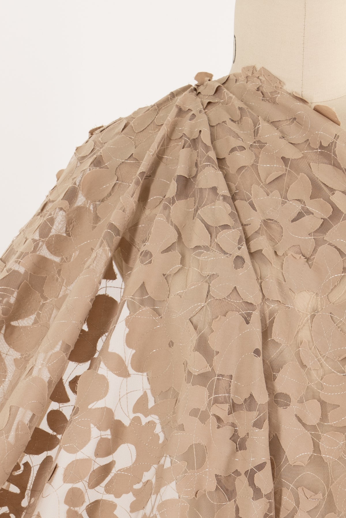 Beige floral lace fabric with leaf cutouts, ideal for apparel and creative sewing projects