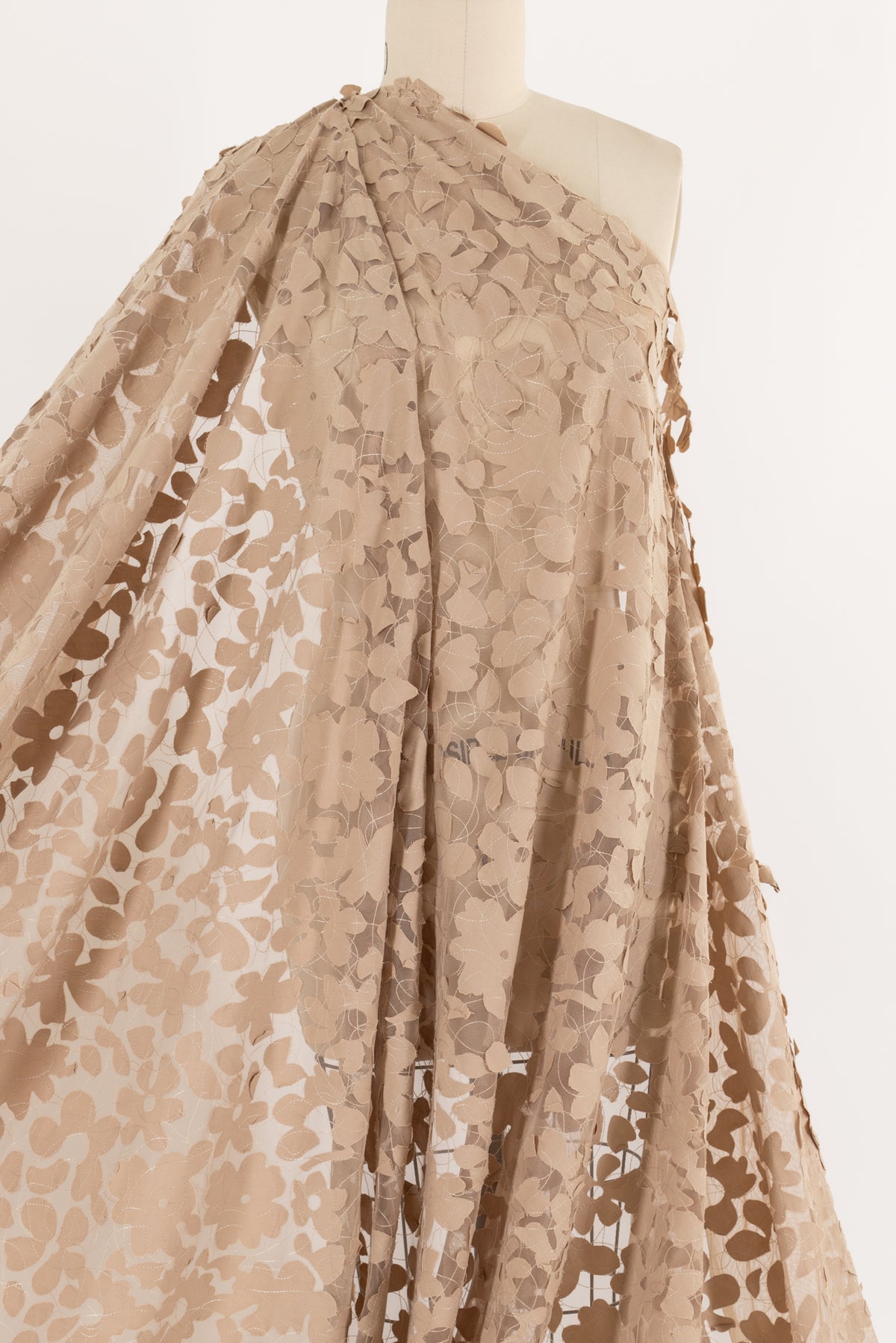 Beige floral lace fabric draped on mannequin, ideal for apparel sewing and fashion projects