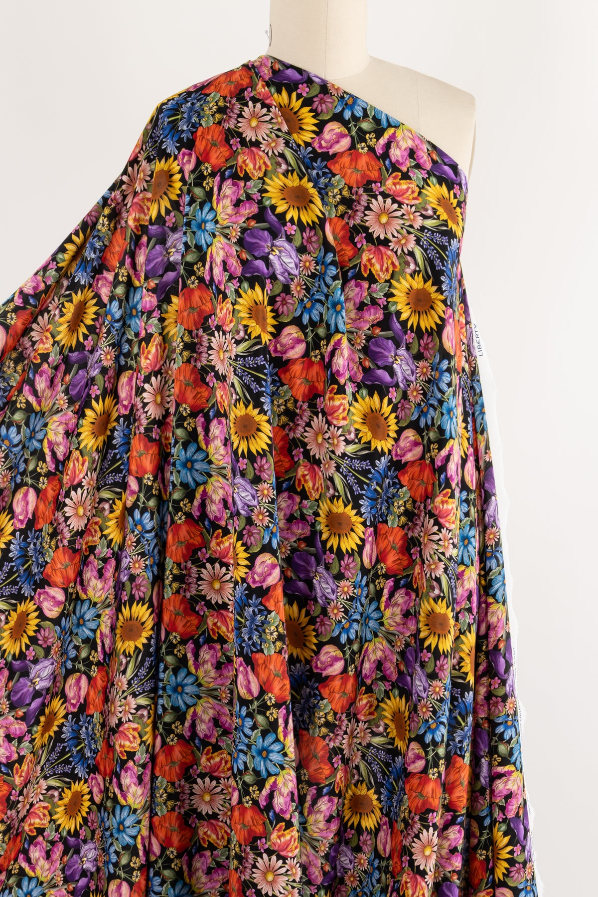 Vibrant floral print fabric with sunflowers, poppies, and daisies on black background, ideal for apparel sewing