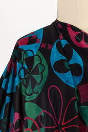 Vibrant abstract floral print fabric in teal, green, and magenta on black background, ideal for apparel sewing.