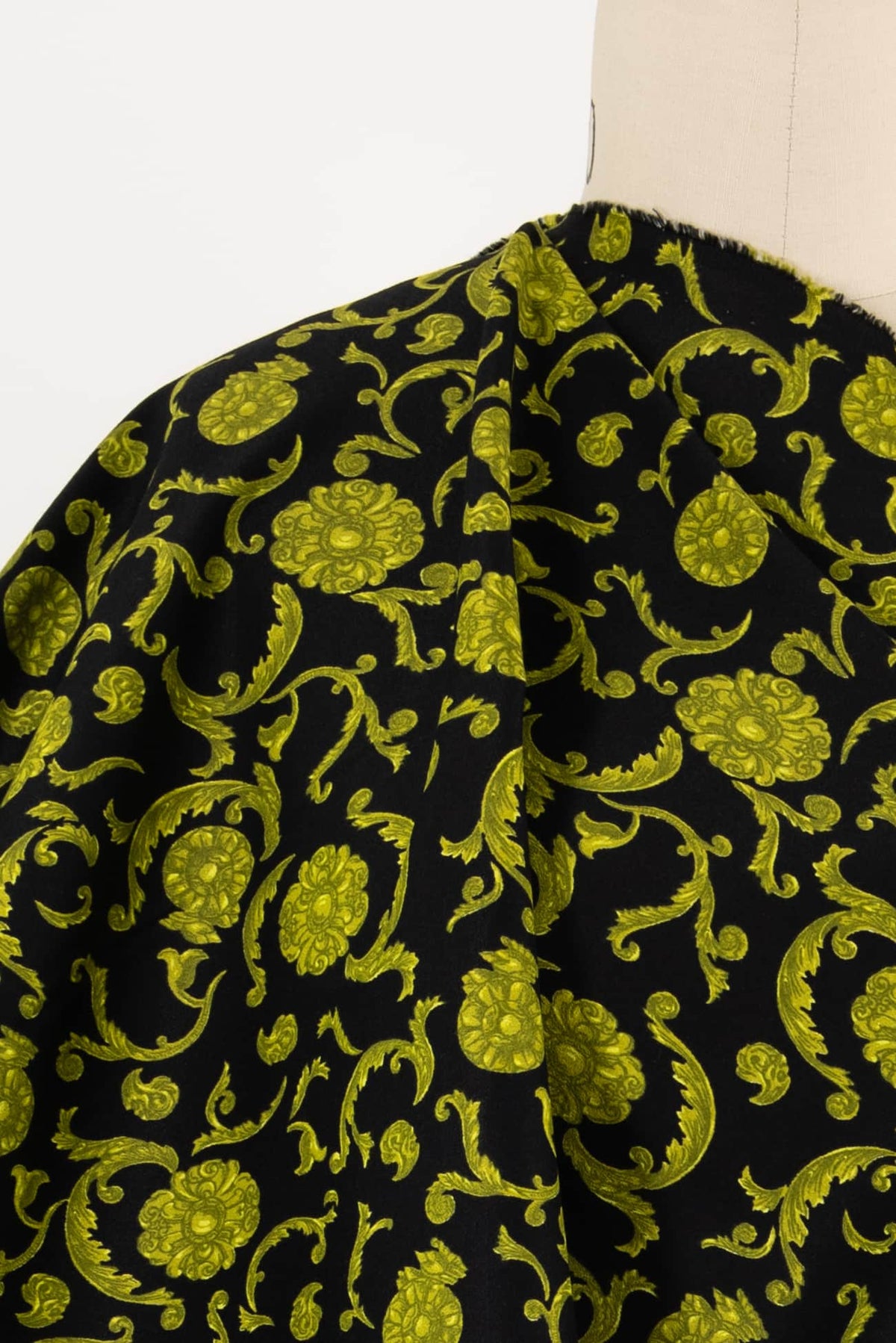 Black fabric with vibrant green floral and scroll print, ideal for apparel and sewing projects
