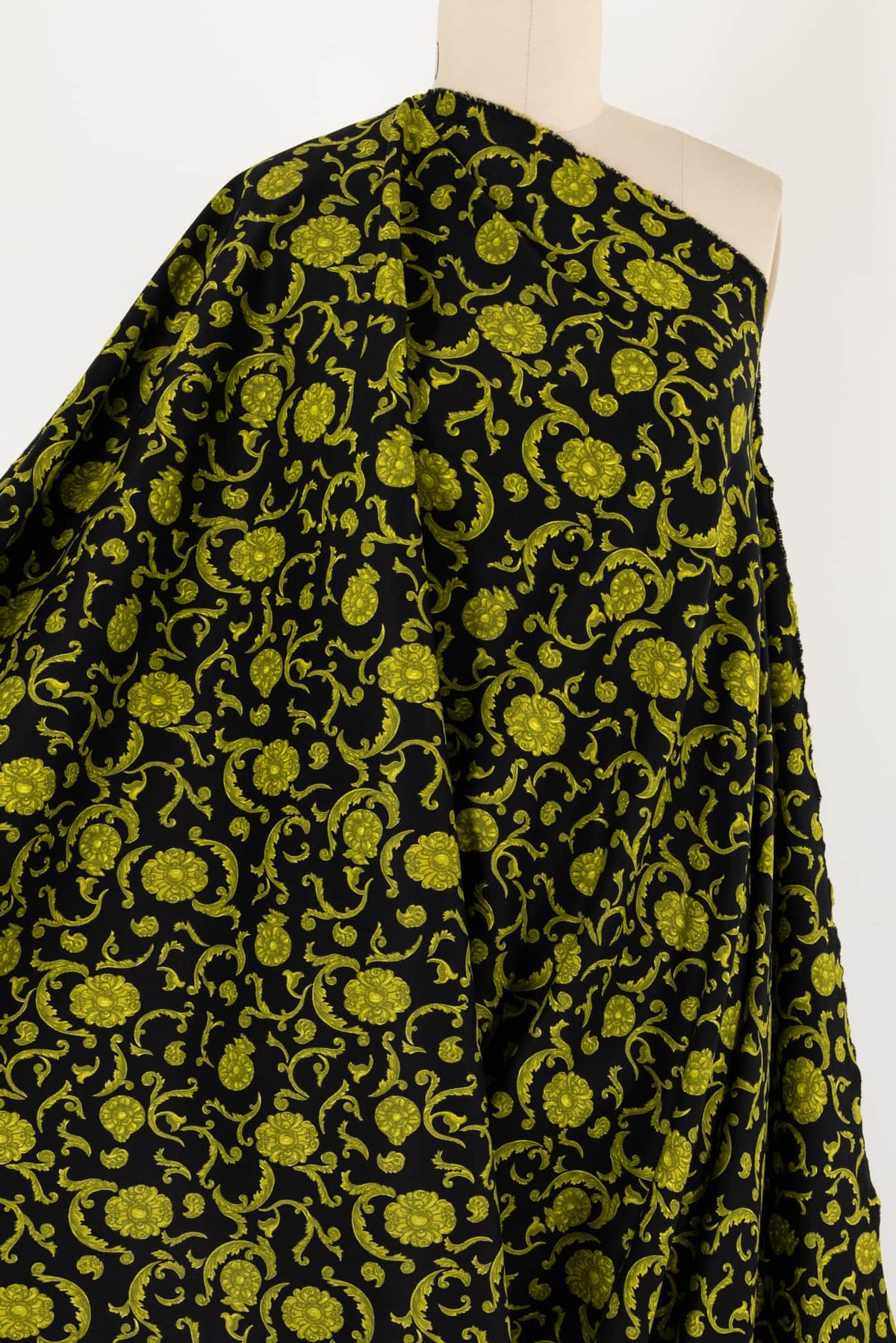Black fabric with vibrant green floral vine print, ideal for apparel sewing and fashion projects.