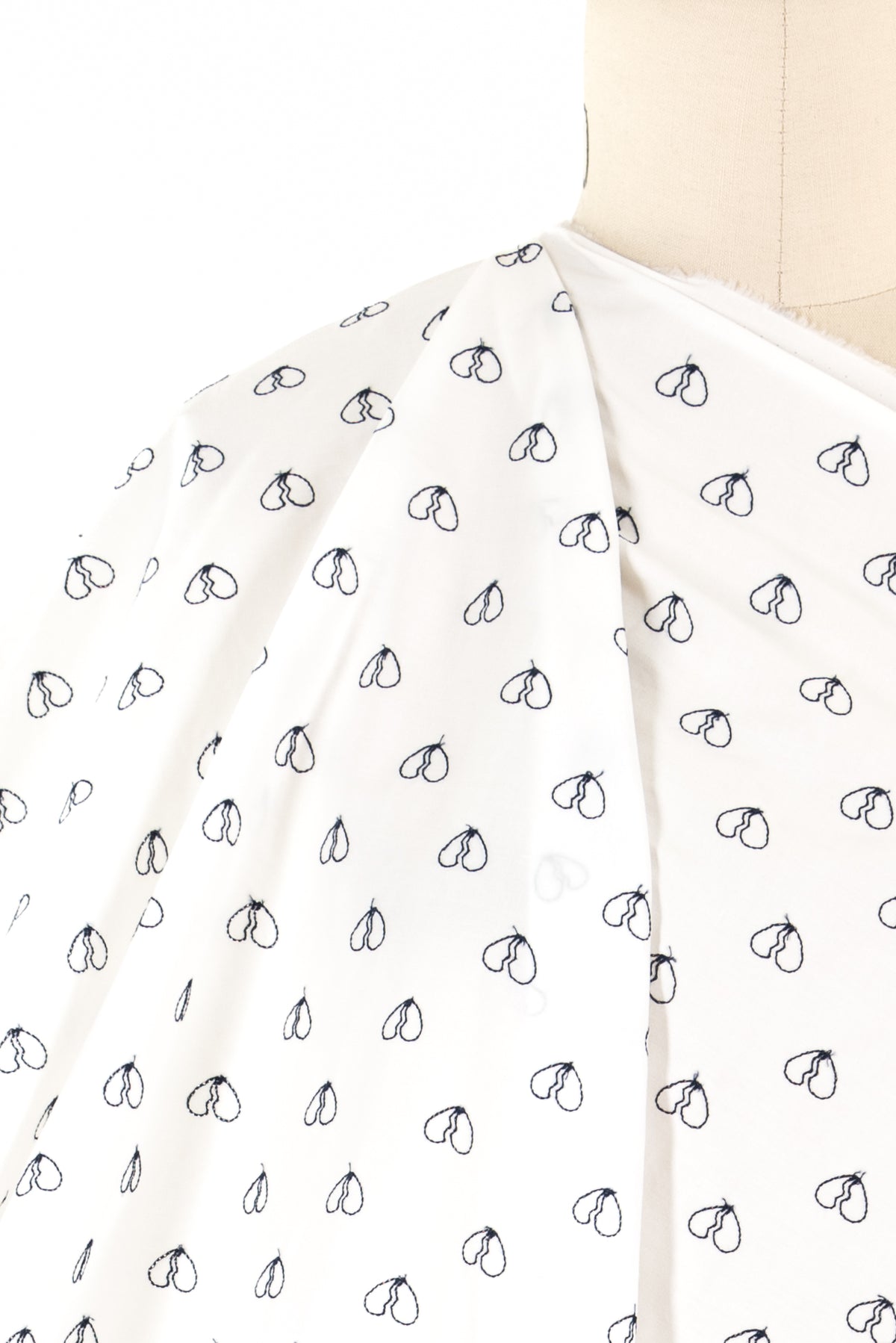 White fabric with black heart print, ideal for sewing apparel or quilting projects