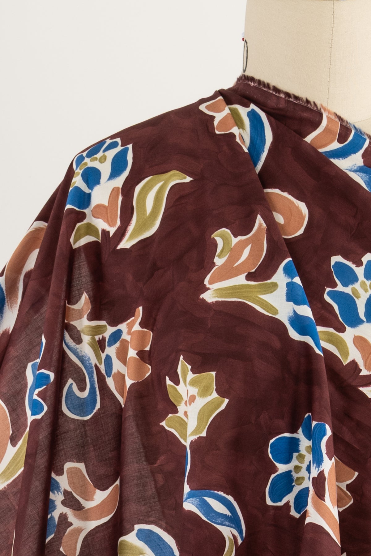 Floral print fabric in burgundy with blue, green, and tan accents draped on mannequin for sewing projects