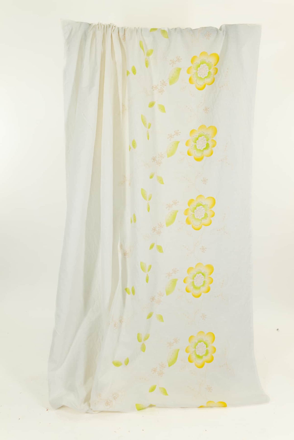 White fabric with yellow floral print and green leaves, ideal for apparel or quilting projects