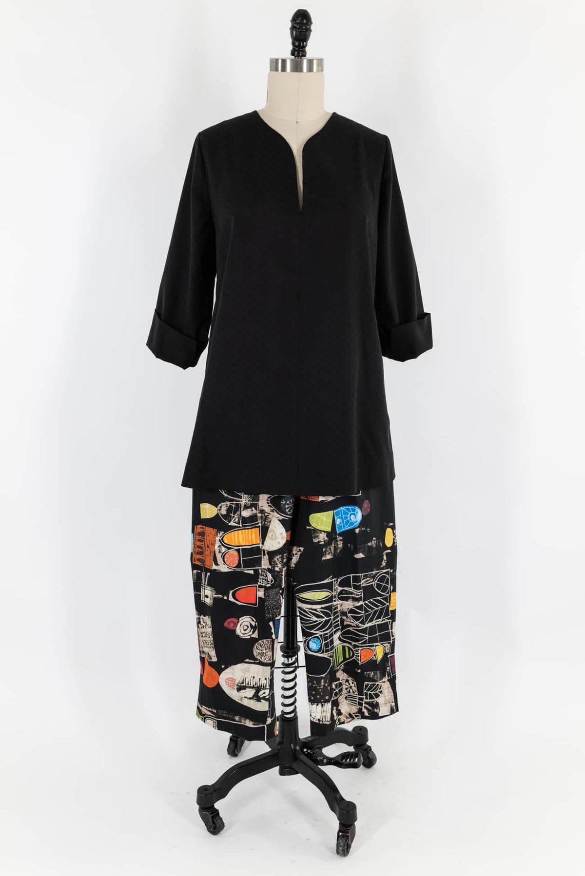 Black V-neck tunic with rolled sleeves paired with abstract print wide-leg pants on mannequin