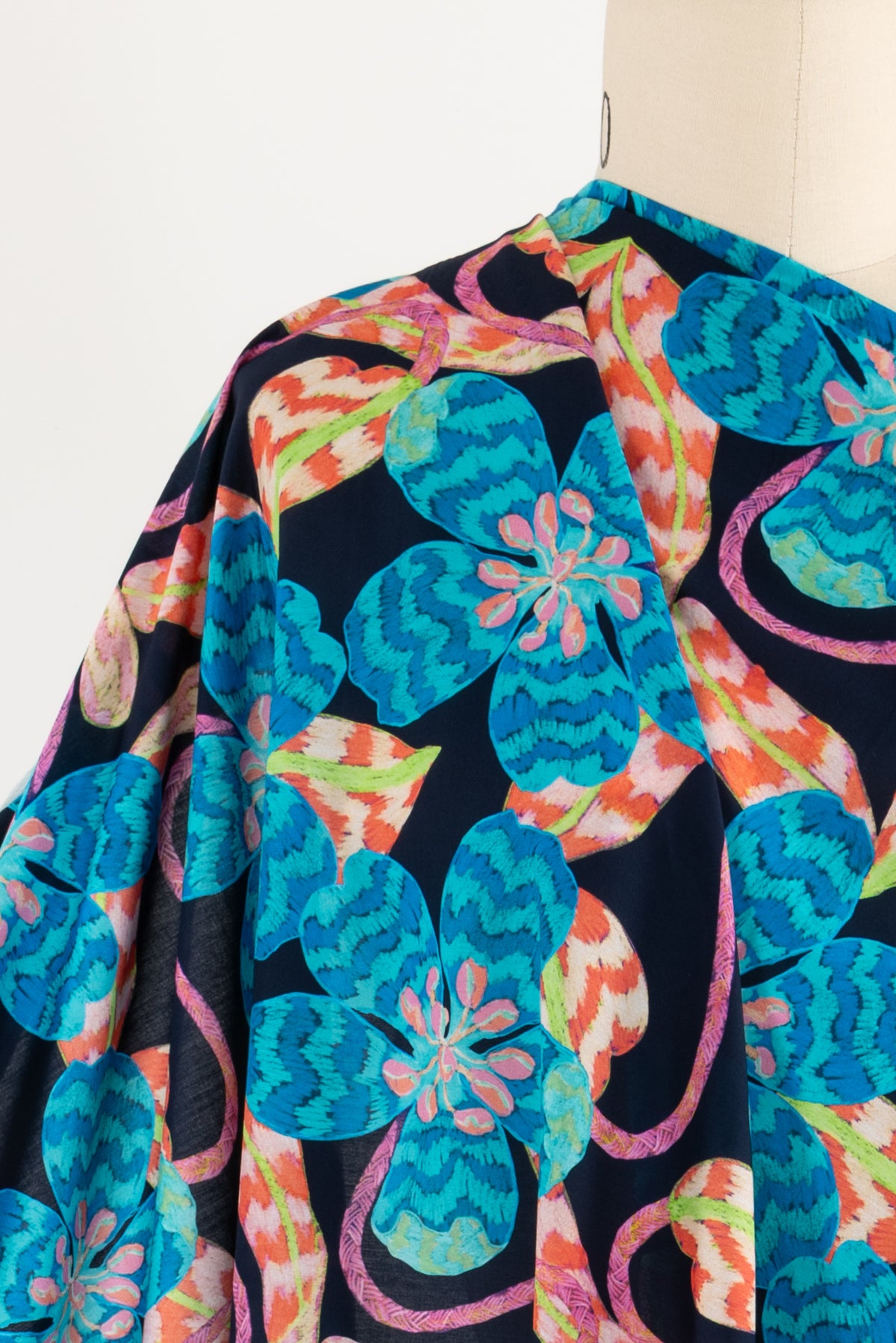 Vibrant floral fabric with teal, orange, and pink patterns on dark background, ideal for apparel sewing.