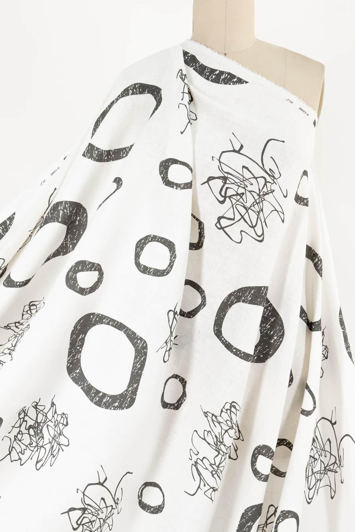 White fabric with black abstract scribble and geometric print, ideal for apparel sewing projects