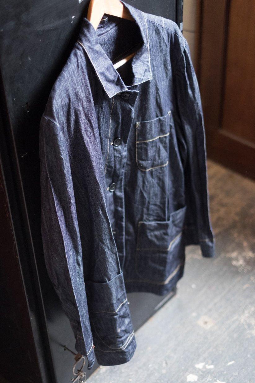 Dark indigo denim shirt with contrast stitching, button front, and chest pockets, hanging on hanger