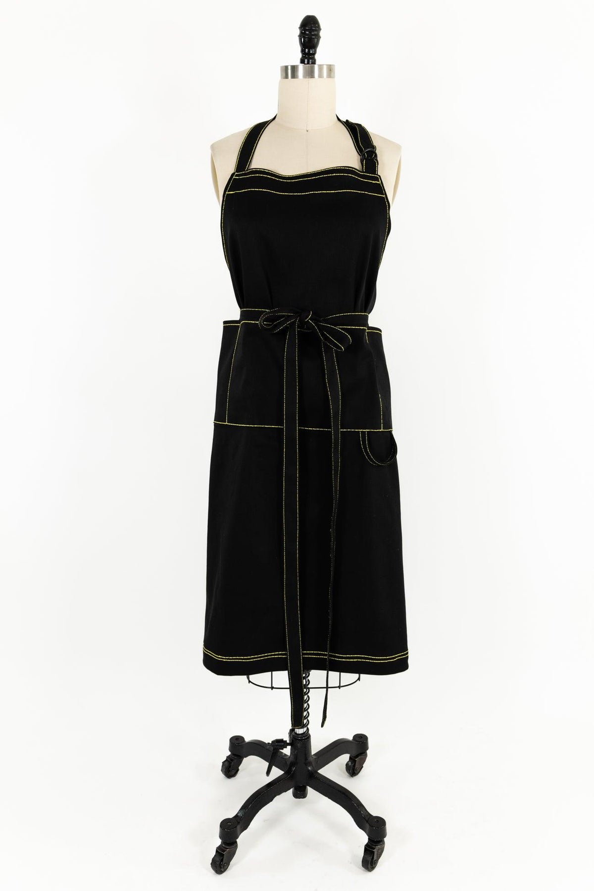 Black apron with yellow contrast stitching, tie waist, and pockets on mannequin — ideal for sewing, crafting, or kitchen use.