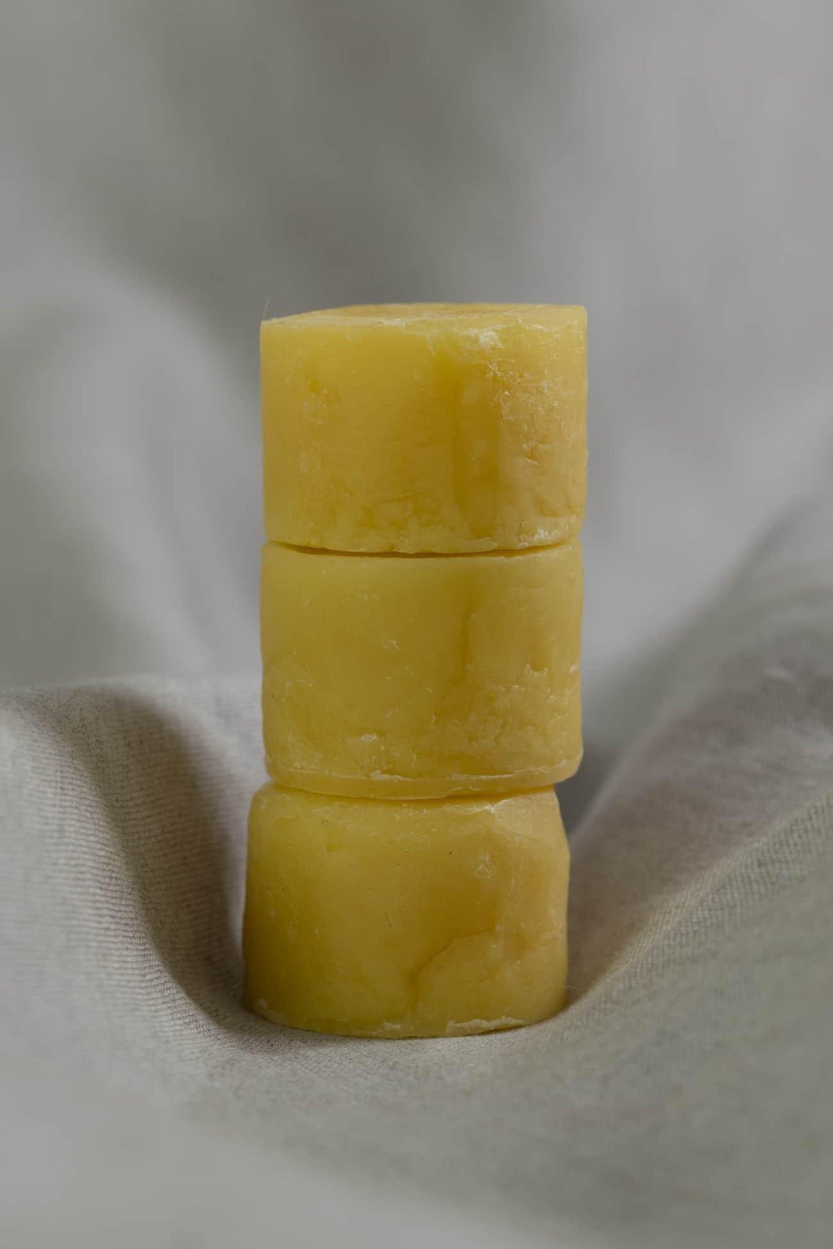 Three yellow beeswax bars stacked on linen fabric for sewing and crafting projects
