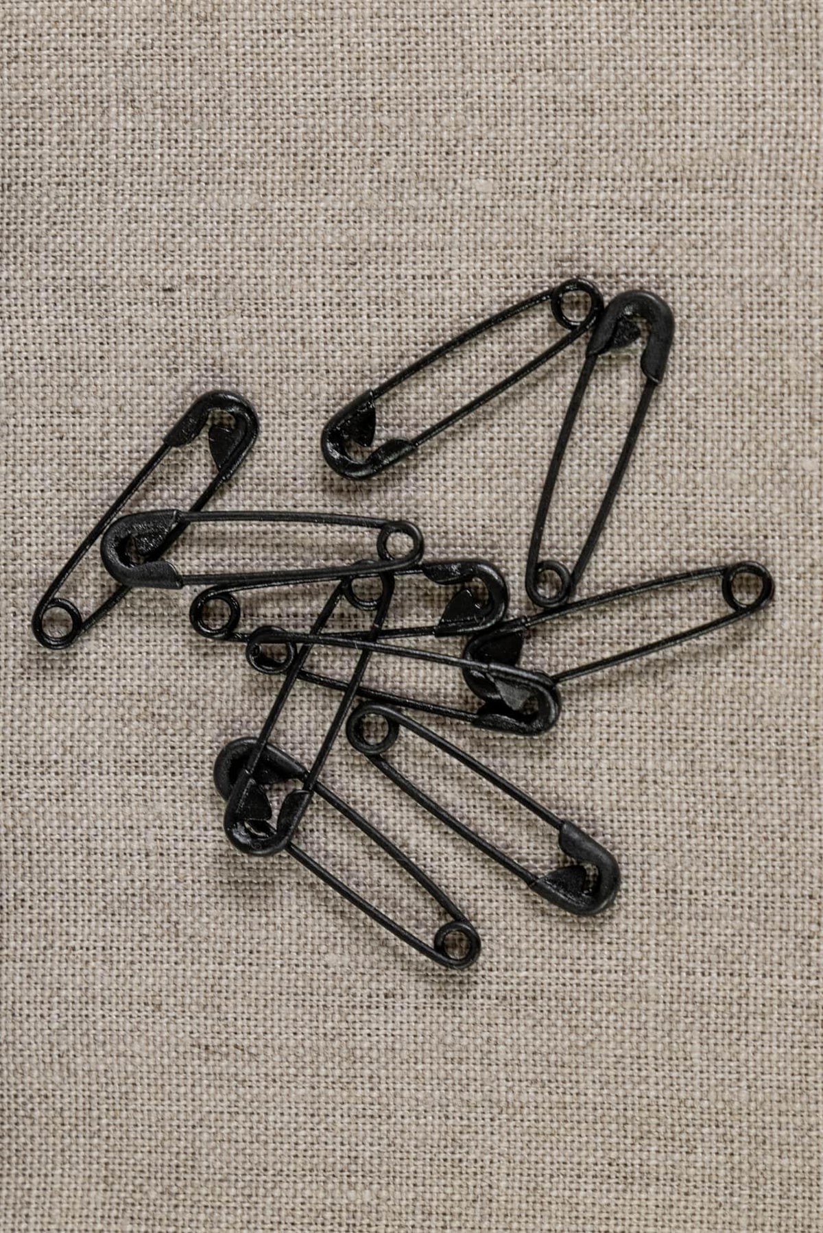 Black safety pins on textured linen fabric for sewing and crafting projects