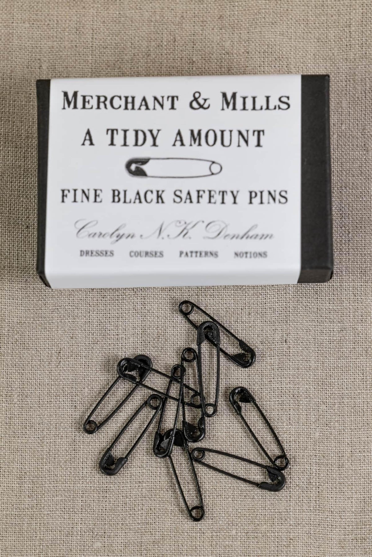 Fine black safety pins by Merchant & Mills, ideal for sewing, dressmaking, and fabric projects on textured linen background