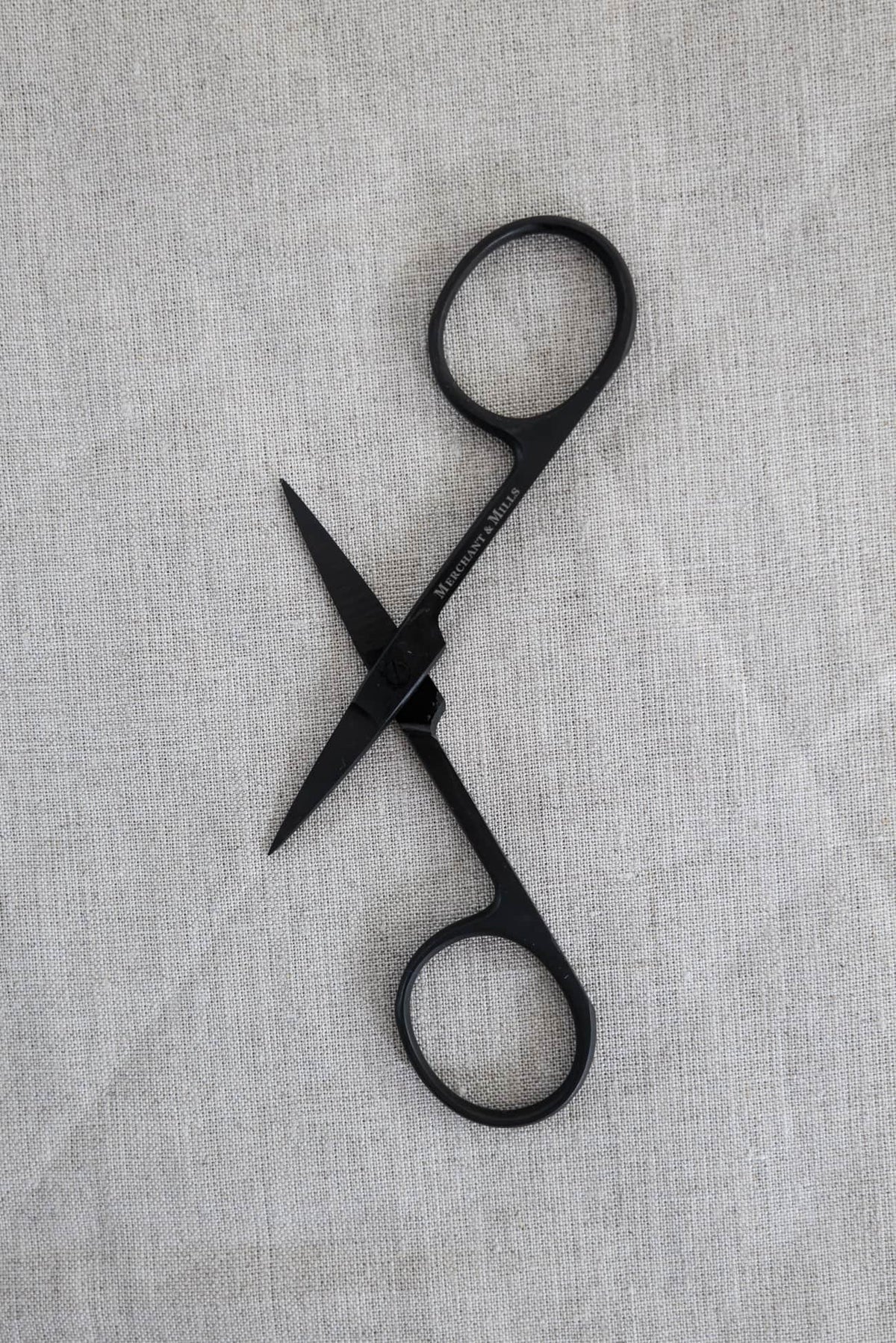 Black Merchant & Mills fabric scissors on neutral linen fabric for sewing and crafting
