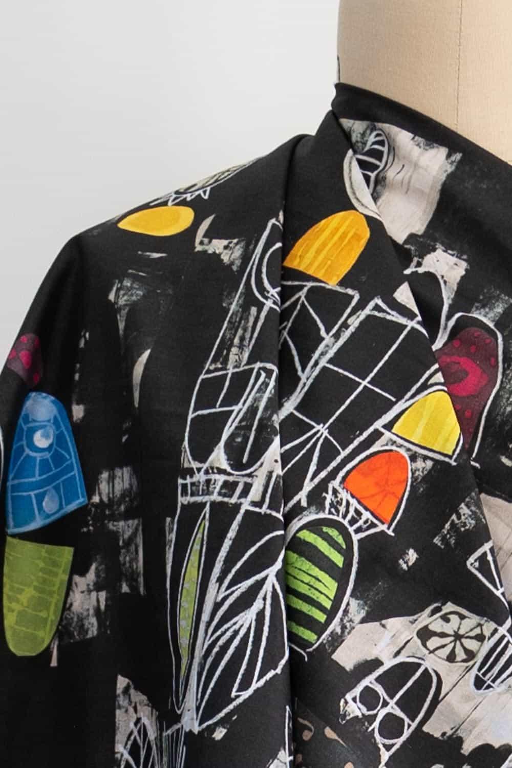 Black abstract print fabric with bold geometric shapes in yellow, blue, green, and red, ideal for apparel sewing