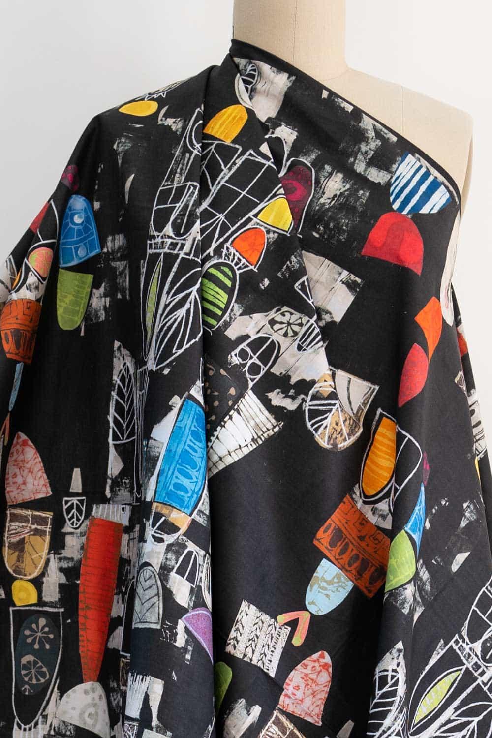 Black fabric with colorful abstract geometric print, ideal for fashion sewing and apparel projects.