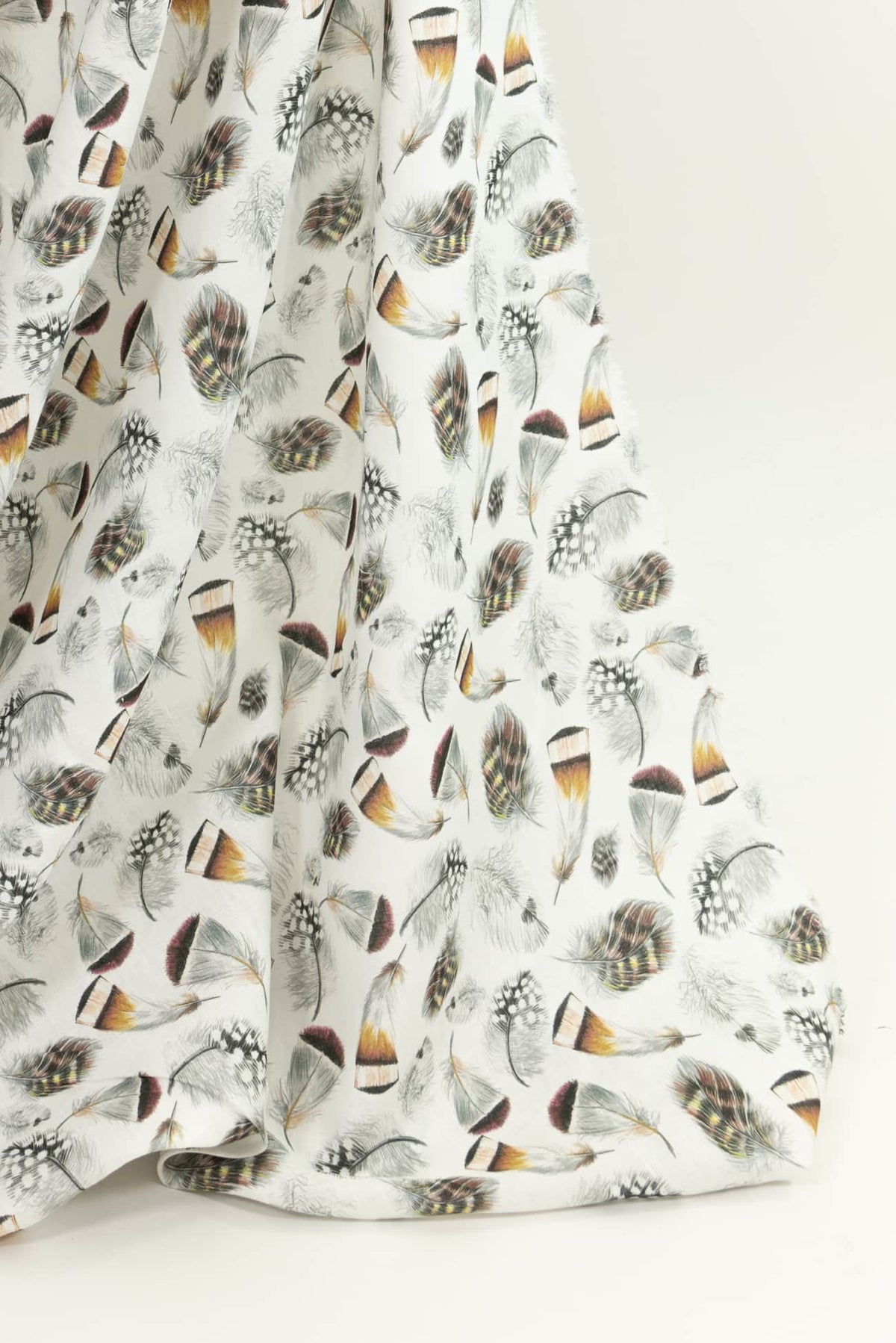 White fabric with colorful feather print, ideal for apparel and sewing projects