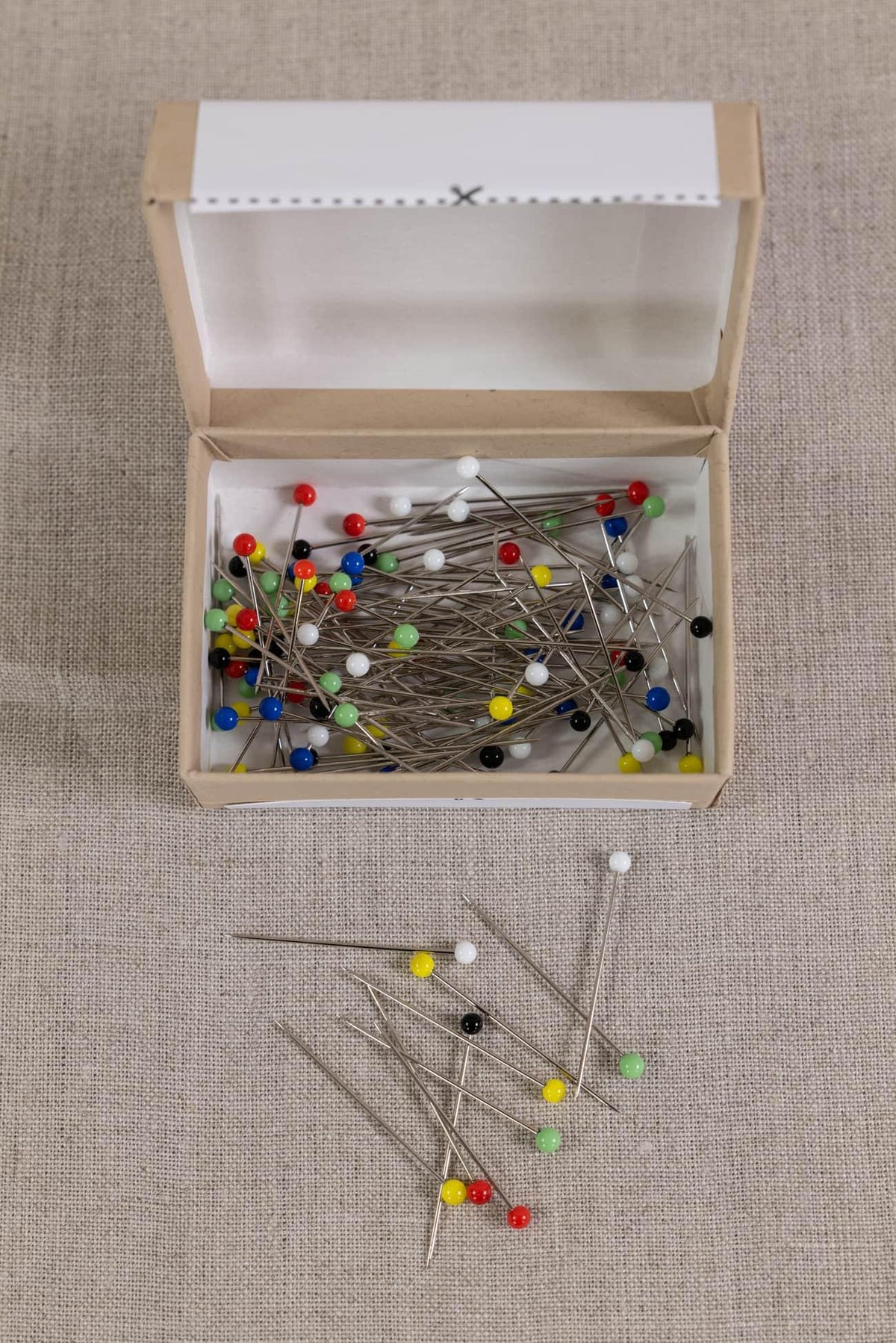 Colorful sewing pins in open box on linen fabric, ideal for quilting and apparel projects