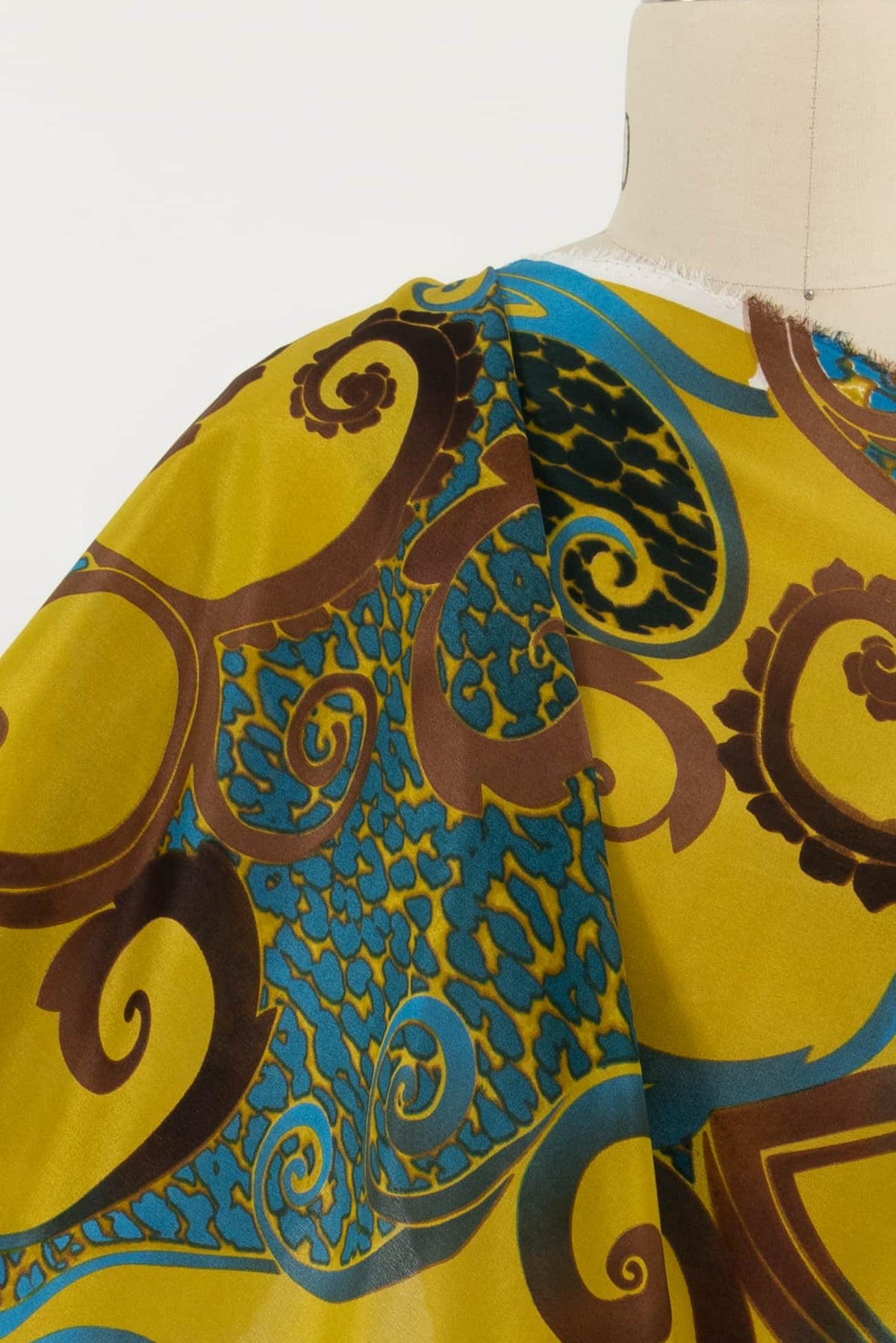 Yellow fabric with blue and brown paisley swirls, draped on mannequin for apparel sewing
