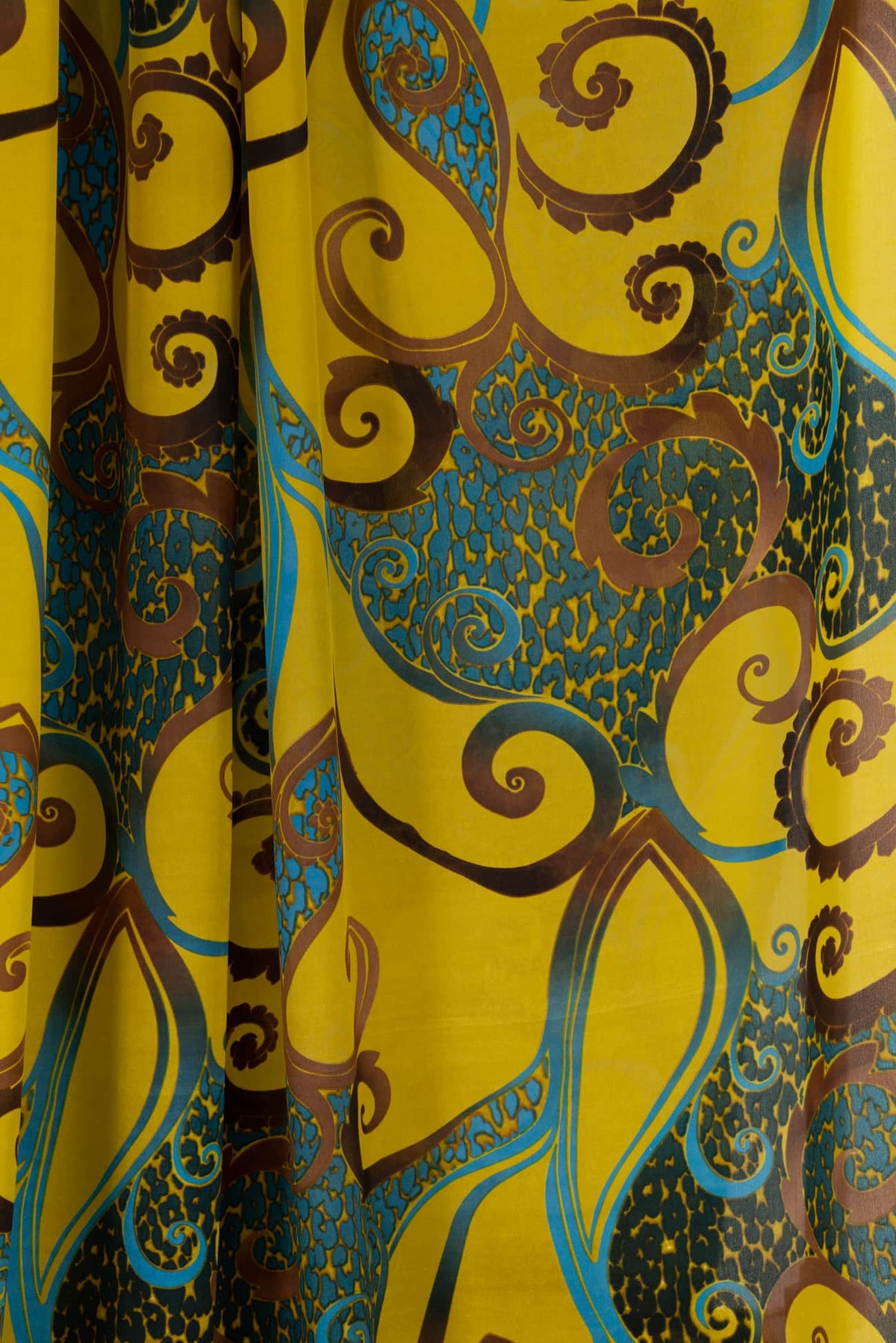 Vibrant yellow fabric with bold blue and brown swirl patterns, ideal for apparel and creative sewing projects.