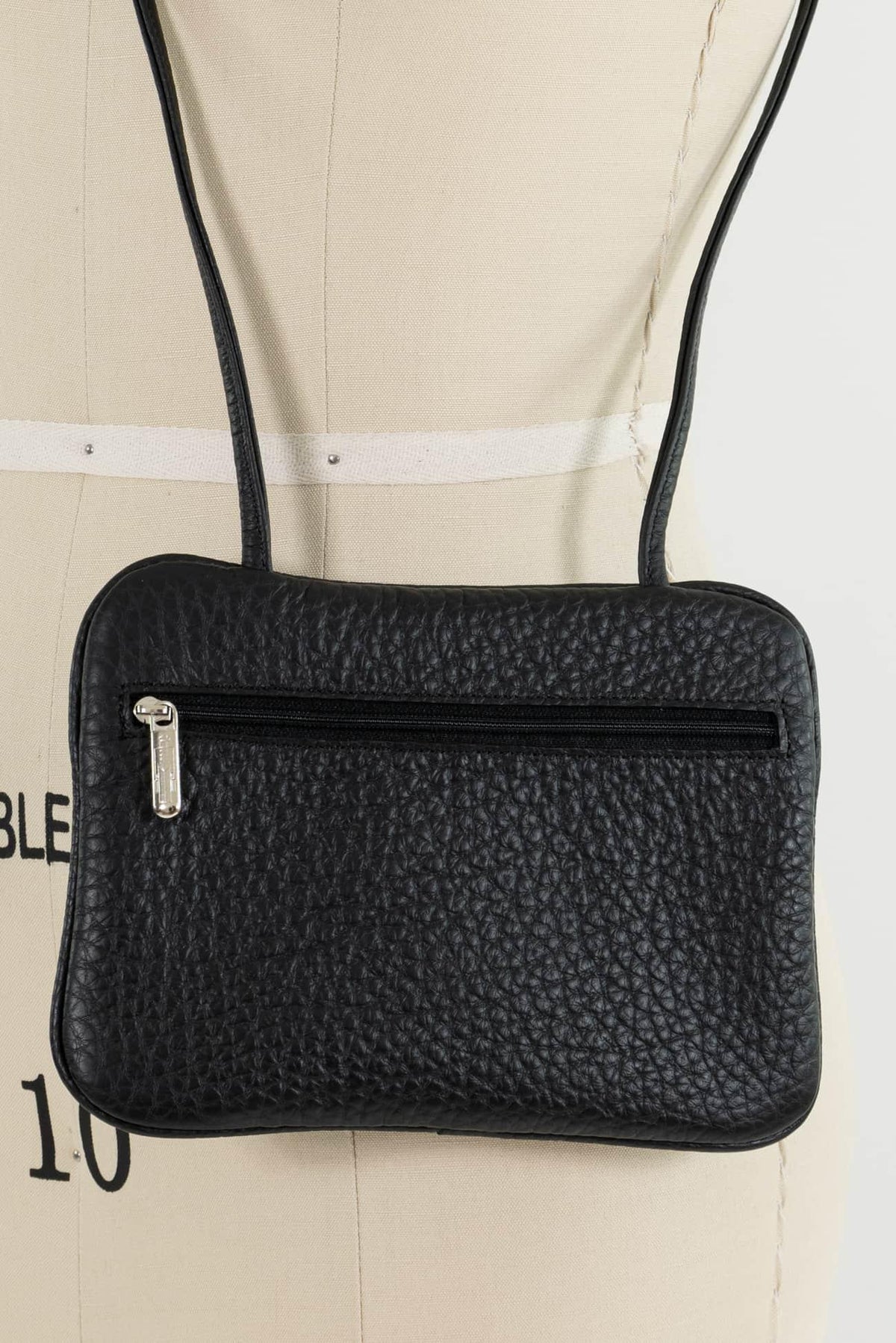 Black textured crossbody bag with front zipper pocket on dress form