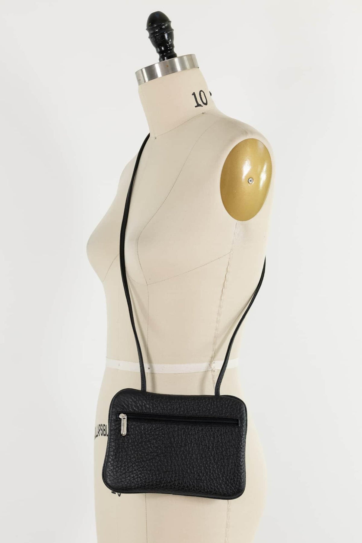 Black textured crossbody bag with zipper, displayed on dress form for sewing or fashion design