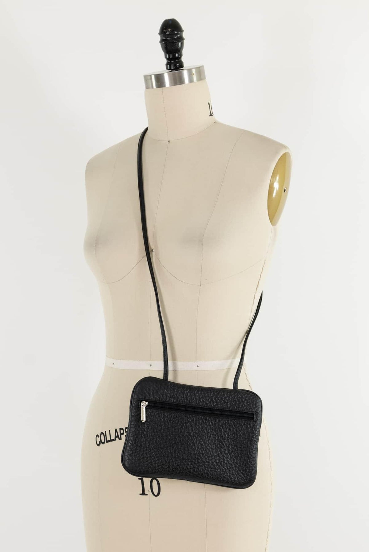 Black textured crossbody bag with zipper on dress form, ideal for sewing and fashion projects