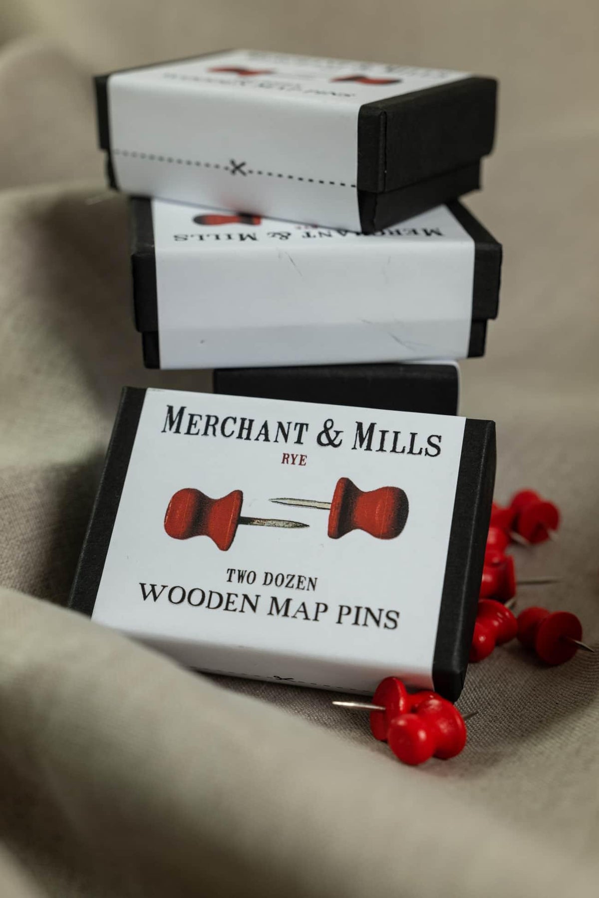 Merchant & Mills Rye wooden map pins in black boxes, red-headed sewing pins scattered on fabric