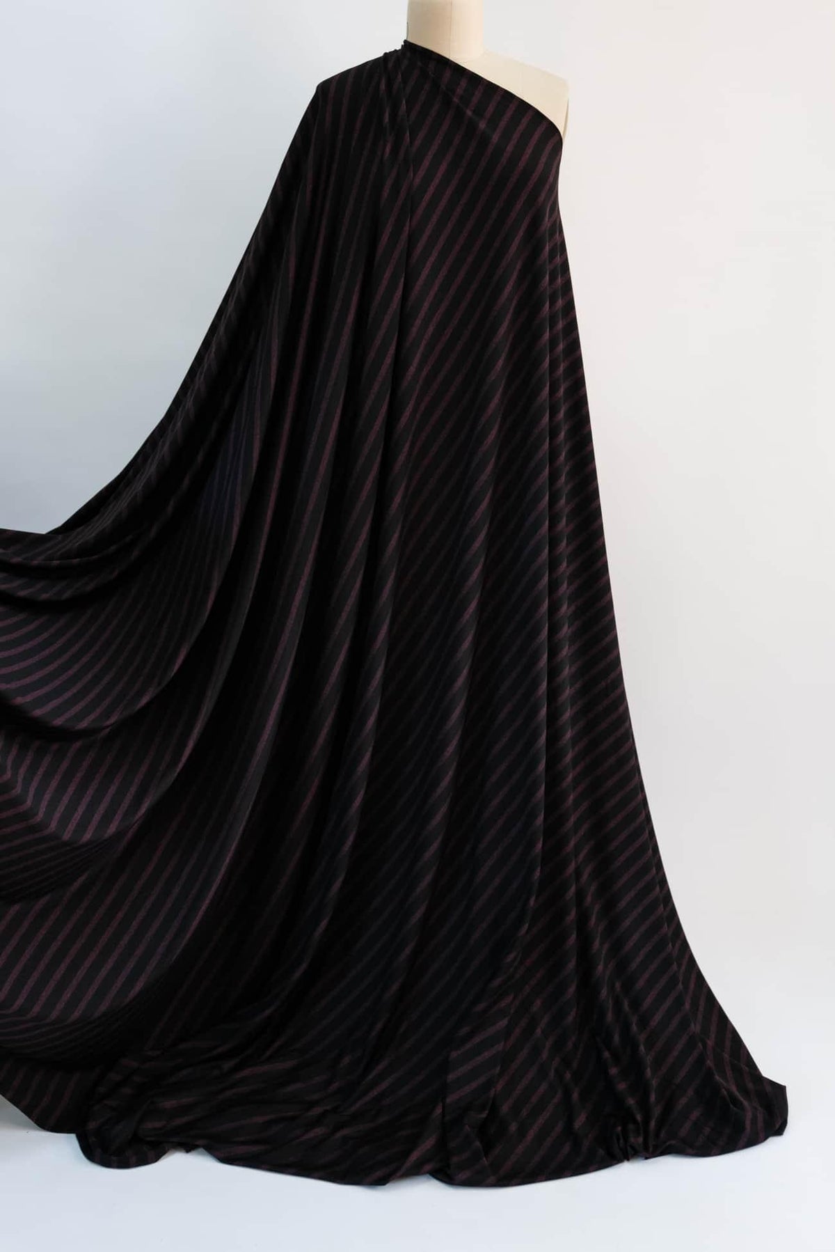 Black fabric with burgundy diagonal stripes, flowing drape on mannequin for apparel sewing
