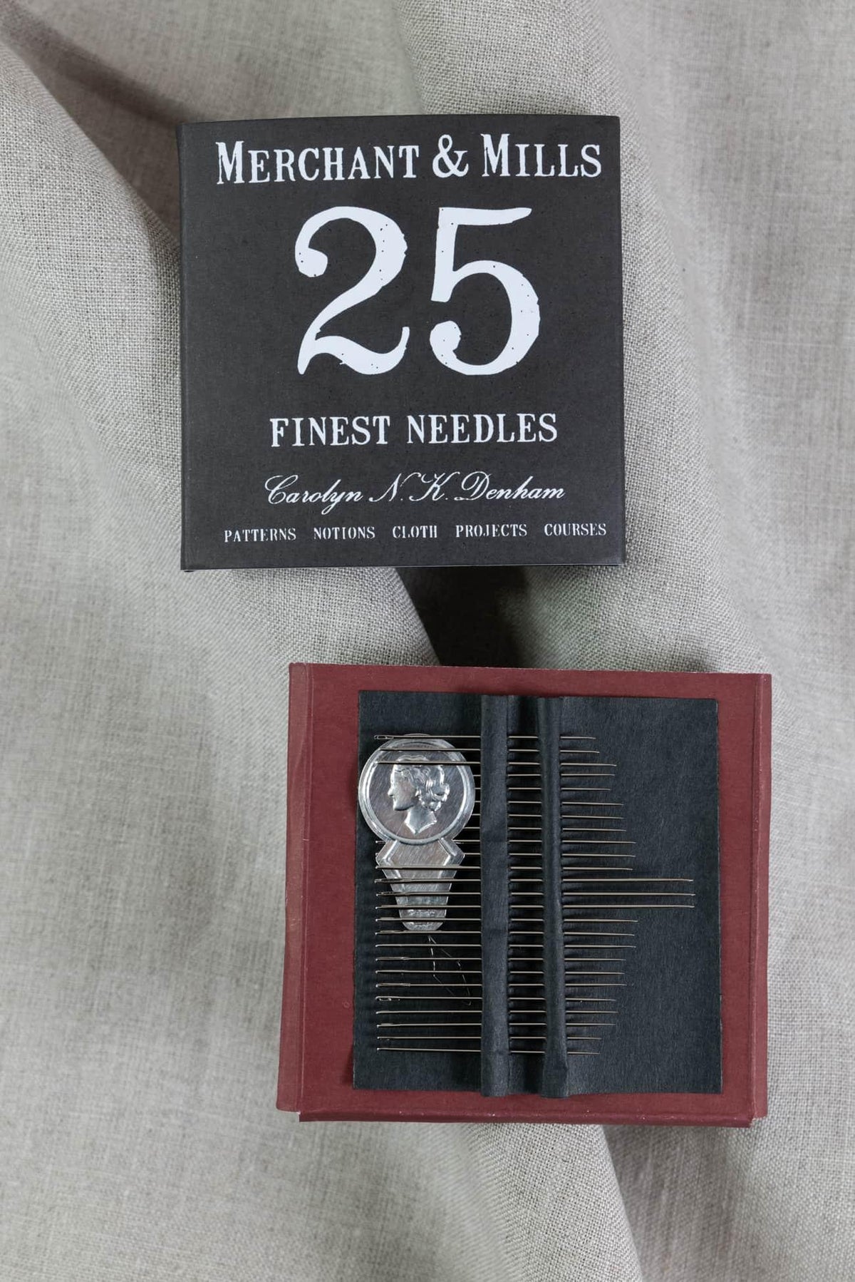 Merchant & Mills 25 finest sewing needles in red box with silver pin, on linen fabric