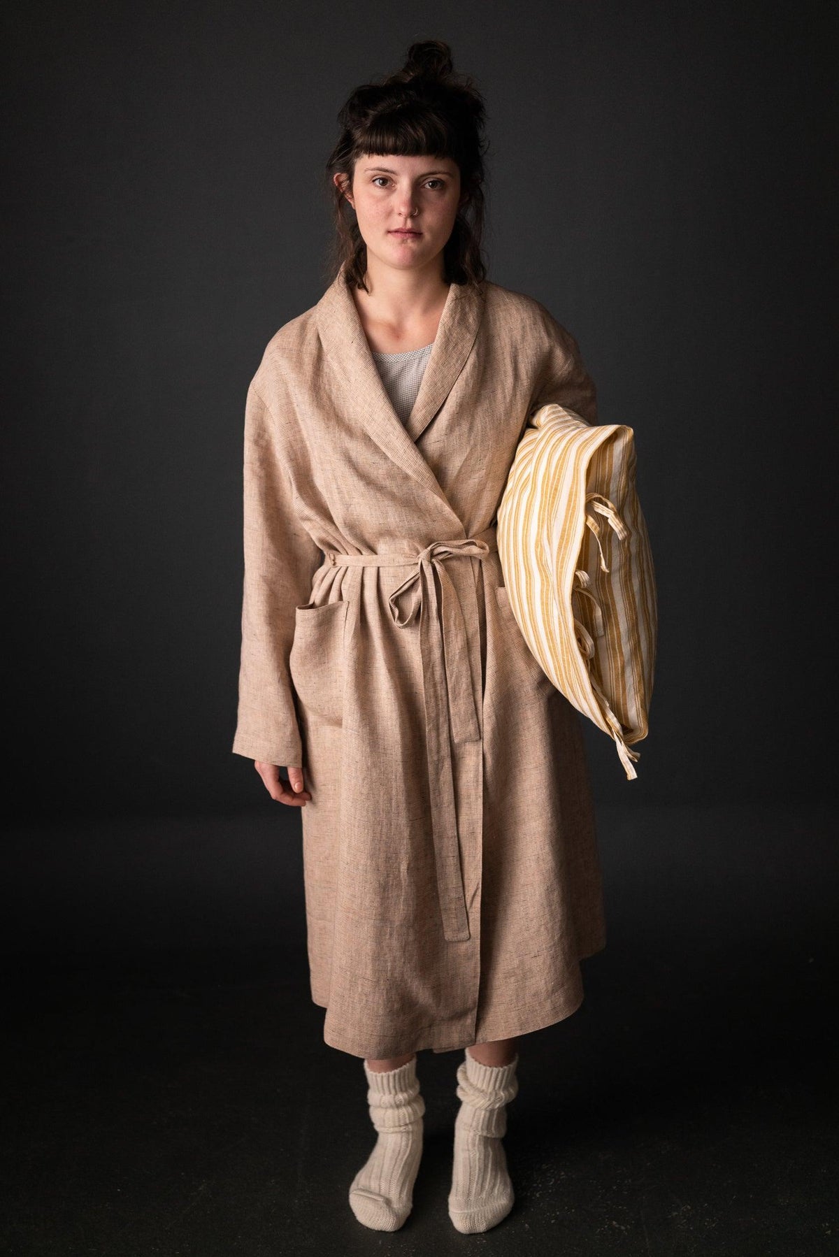 Woman in beige linen wrap coat with striped tote, cozy knit socks, ideal for sewing apparel or quilting projects