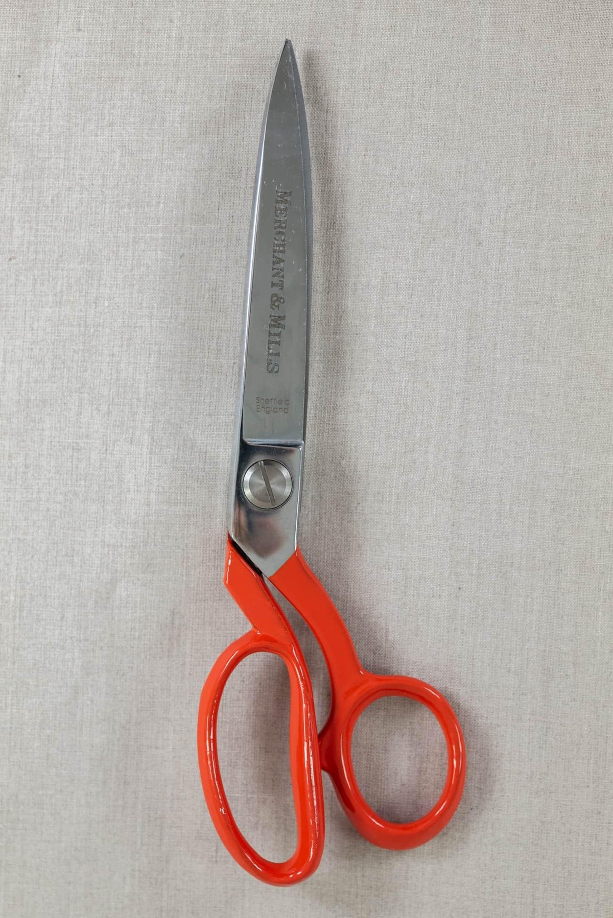 Red-handled fabric scissors on neutral textile background, ideal for sewing and cutting cotton, linen, or knit fabrics.