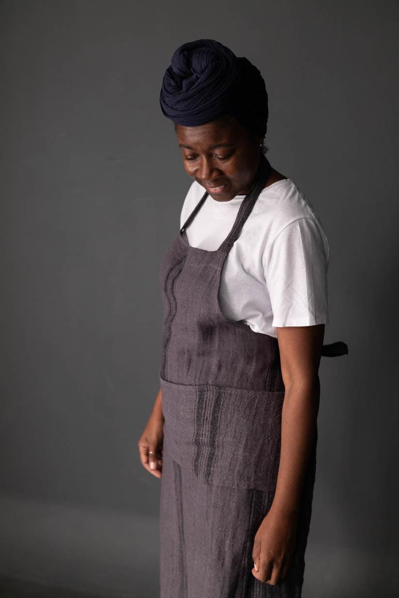 Woman wearing a dark linen apron over white tee, styled with headwrap — ideal for sewing, crafting, or apparel projects.