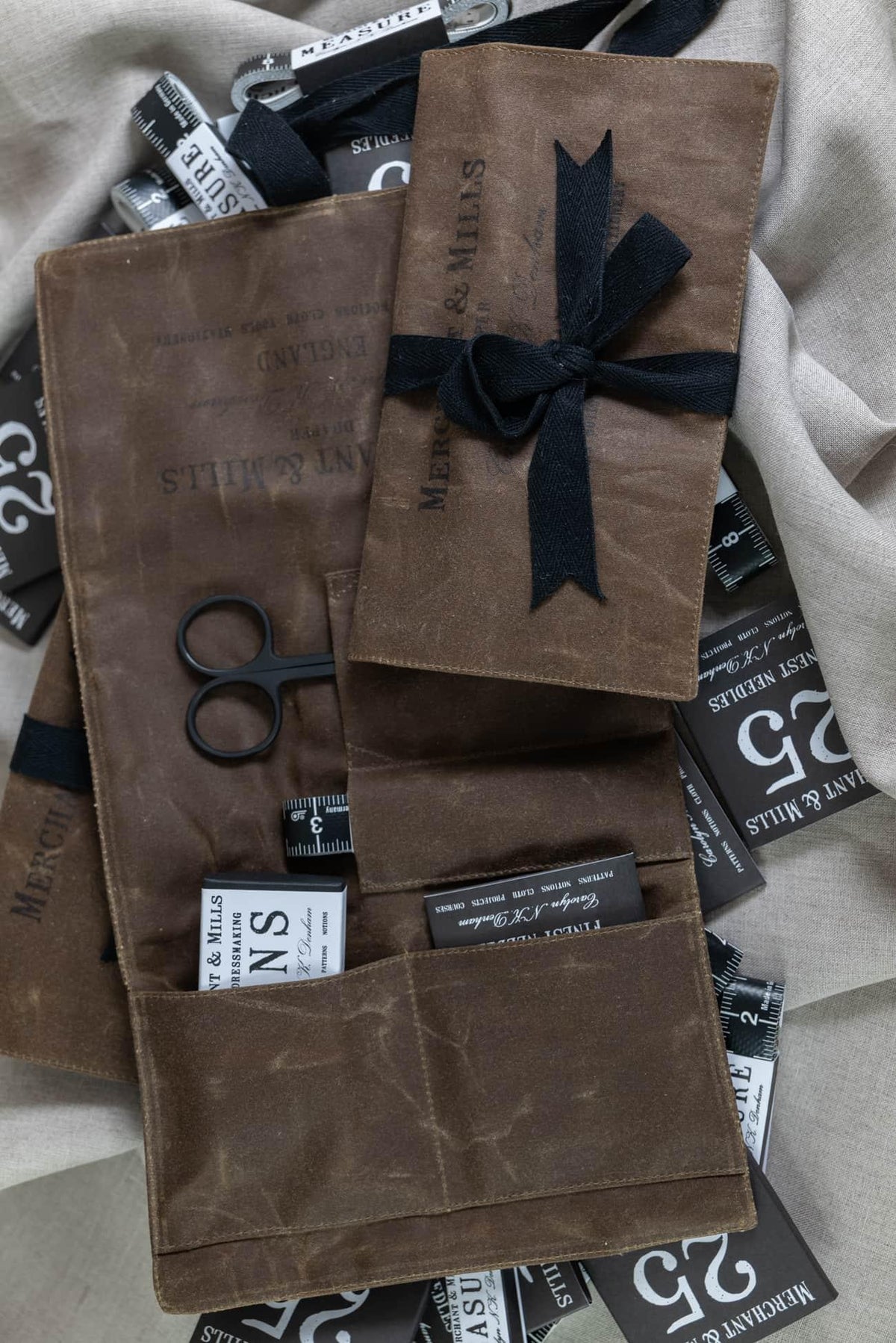 Brown waxed canvas sewing kit with scissors, tape measure, needles, and Merchant & Mills branding