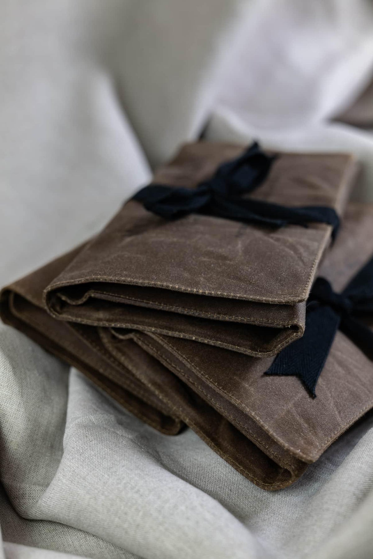 Folded brown waxed canvas fabric bundles tied with navy ribbon, ideal for apparel and sewing projects