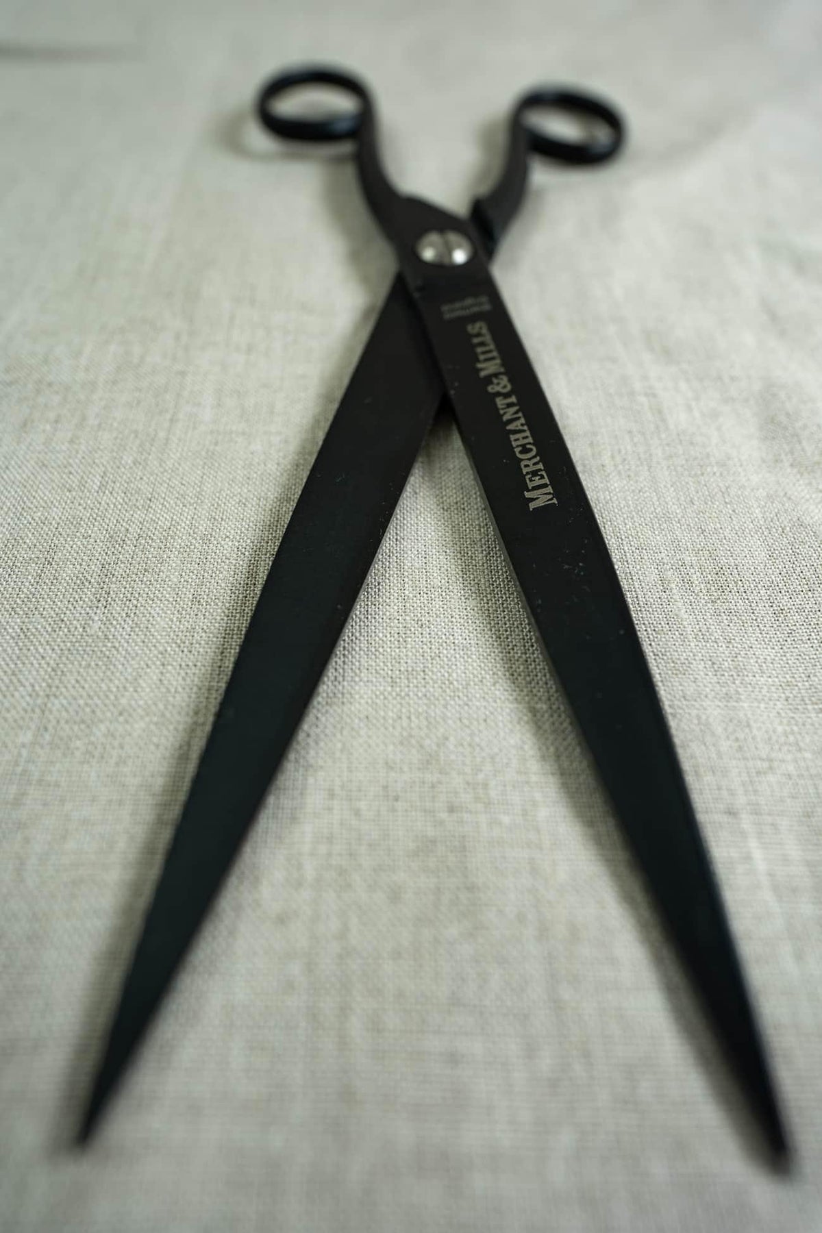 Black fabric shears on neutral linen fabric, ideal for sewing and quilting projects