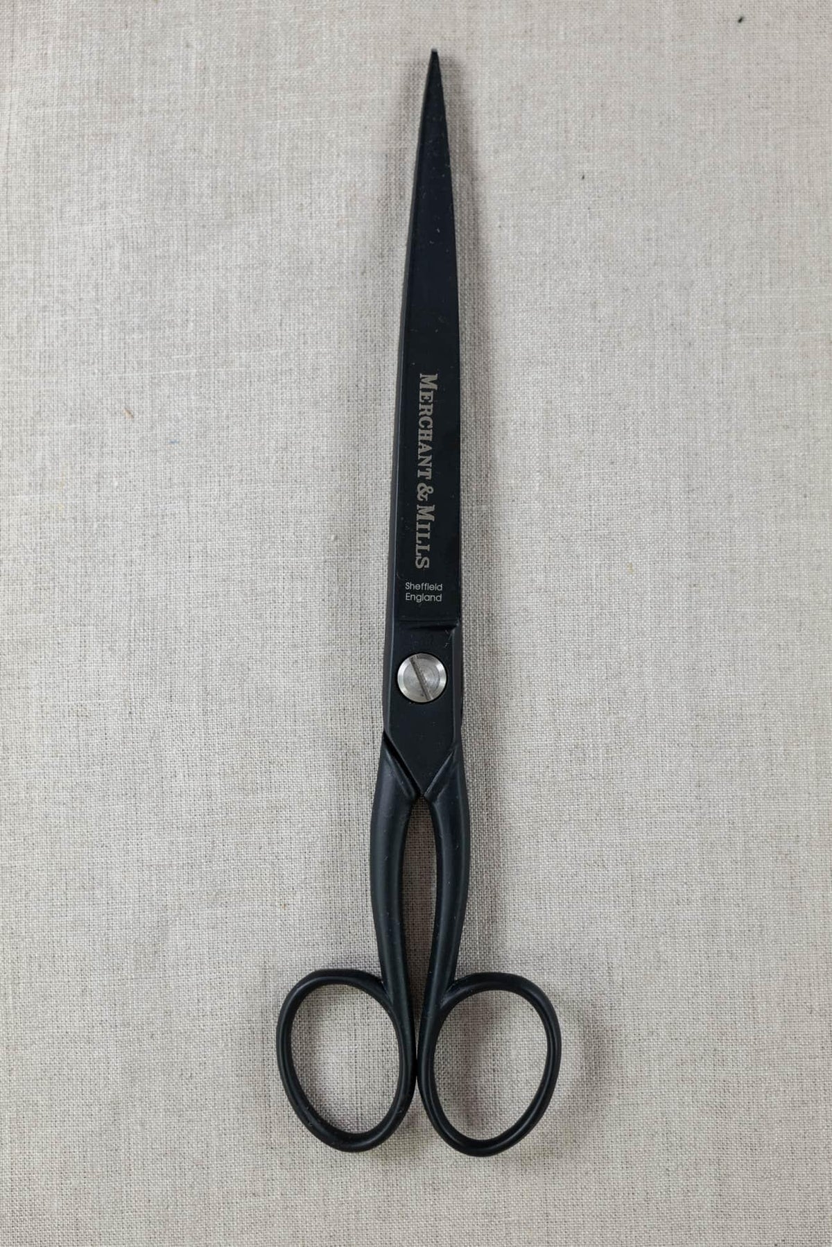 Black Merchant & Mills fabric scissors on neutral linen background for sewing and tailoring projects