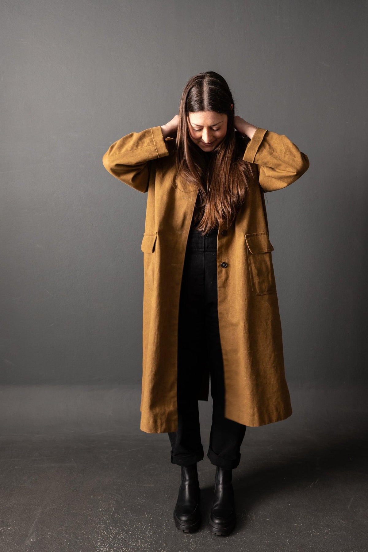 Woman wearing mustard yellow linen coat with pockets, black pants, and boots, styled for fall fashion sewing projects.